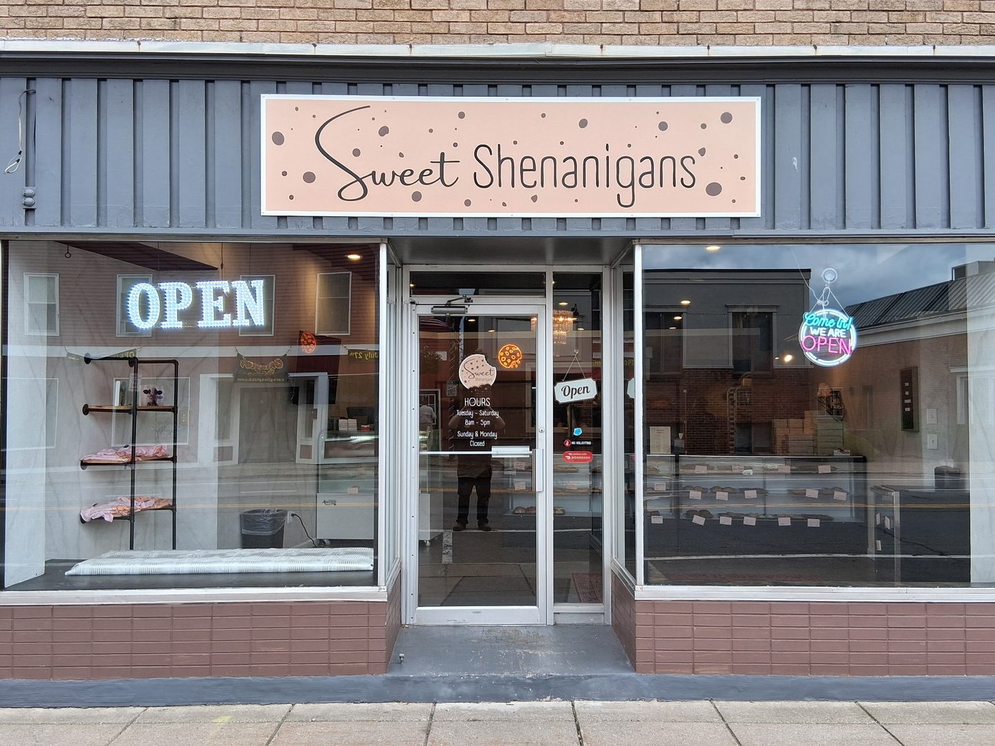 The Sweet Shenanigans storefront at 15 East Main Street in Webster, with the sign above the window and the open sign lit